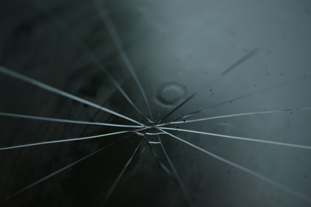 A close-up, high-contrast shot of a spiderweb-style crack on a car windshield, illustrating auto glass damage.